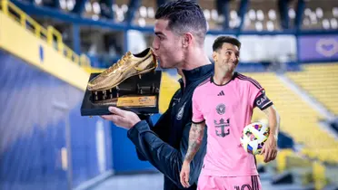 Cristiano Ronaldo kisses his goalscoring award while Lionel Messi smiles and holds a football.