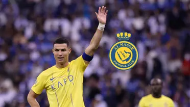 Cristiano Ronaldo lifts his hand up while wearing the Al Nassr jersey and the Al Nassr badge is next to him. (Source: Al Nassr Zone X) 