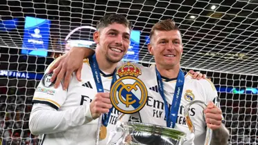 Fede Valverde and Toni Kroos smiles while holding the Champions League trophy and the Real Madrid logo is in the middle.