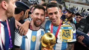 Lionel Messi and Angel Di Maria pose for a picture together with the World Cup trophy and the Argentina national team badge is next to them.