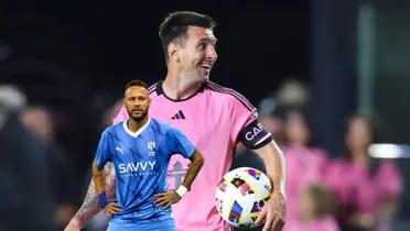 Lionel Messi grabs the ball with a smile on his face and wearing the Inter Miami jersey while Neymar looks concerned by holding