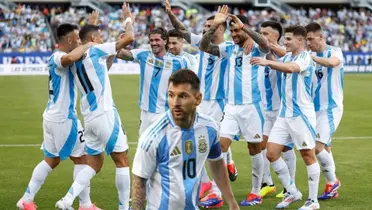 Lionel Messi looks to the side while wearing the Argentina jersey and the rest of the Argentina national team are celebrating together.