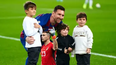 Lionel Messi poses for a picture with his children while Emiliano Martinez points up while wearing the Argentina national team goalkeeper kit.