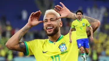 Neymar does a celebration with his hands wearing the Brazil kit while Marquinhos also wears the Brazil kit.