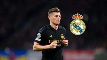 Toni Kroos jogs while wearing the black Real Madrid jersey and the Real Madrid crest is next to him.