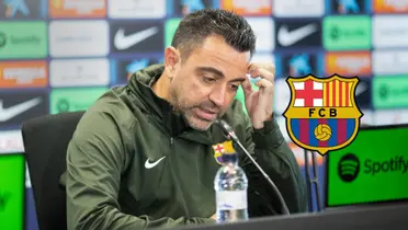 Xavi Hernandez scratches his head during a press conference while the FC Barcelona badge is next to him.