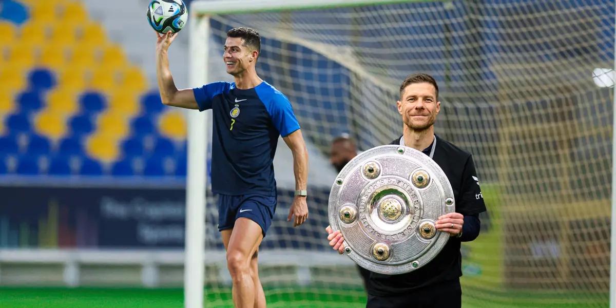 Cristiano Ronaldo holds the ball with one hand wearing a training Al Nassr kit while Xabi Alonso holds the Bundesliga title.