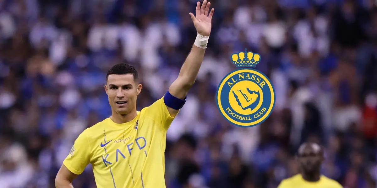 Cristiano Ronaldo lifts his hand up while wearing the Al Nassr jersey and the Al Nassr badge is next to him. (Source: Al Nassr Zone X)